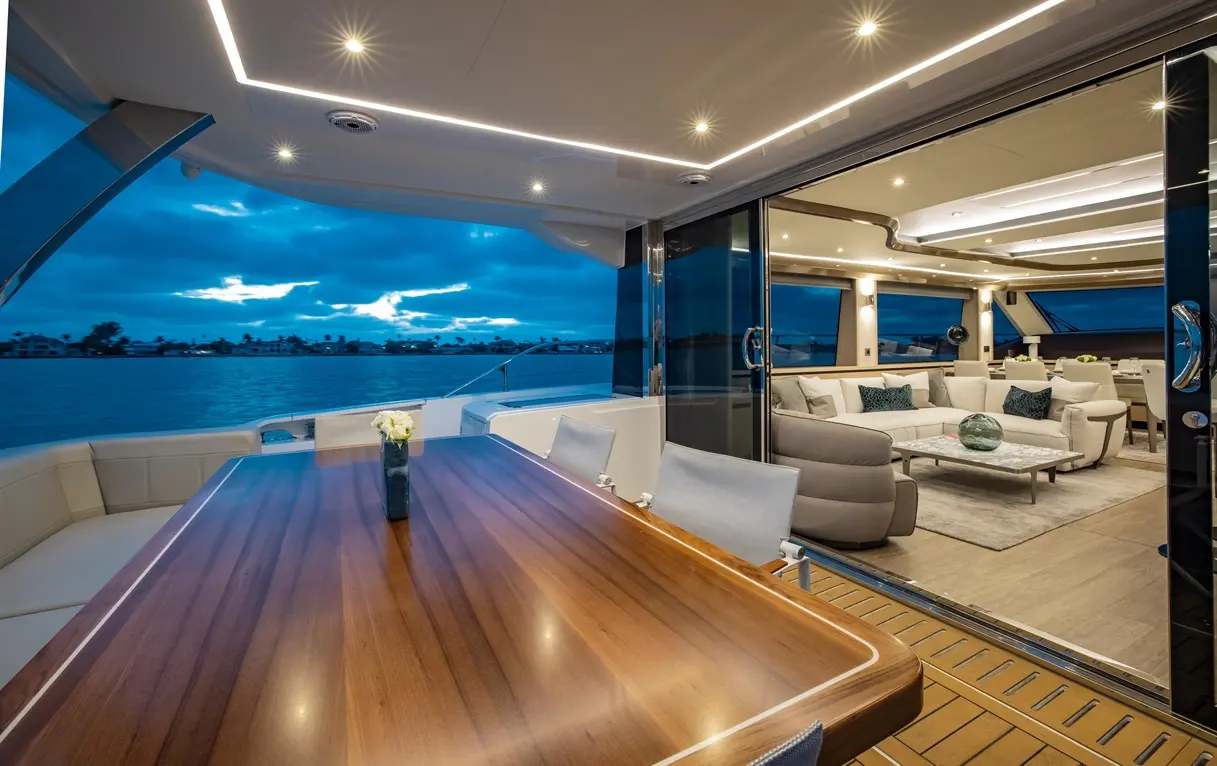 Elegant yacht interior with a dining table and lounge area, overlooking water and dramatic evening sky.